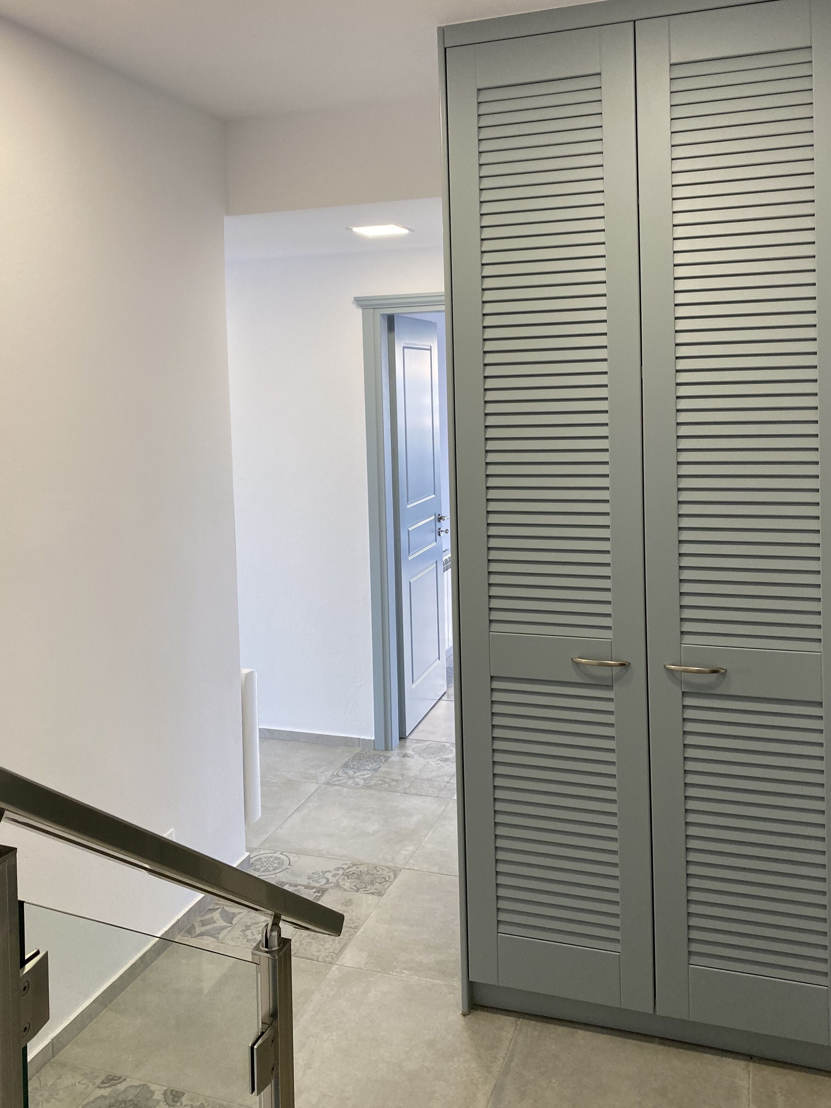 A hallway with a closed grey wardrobe, a white door at the end, and a tiled floor.