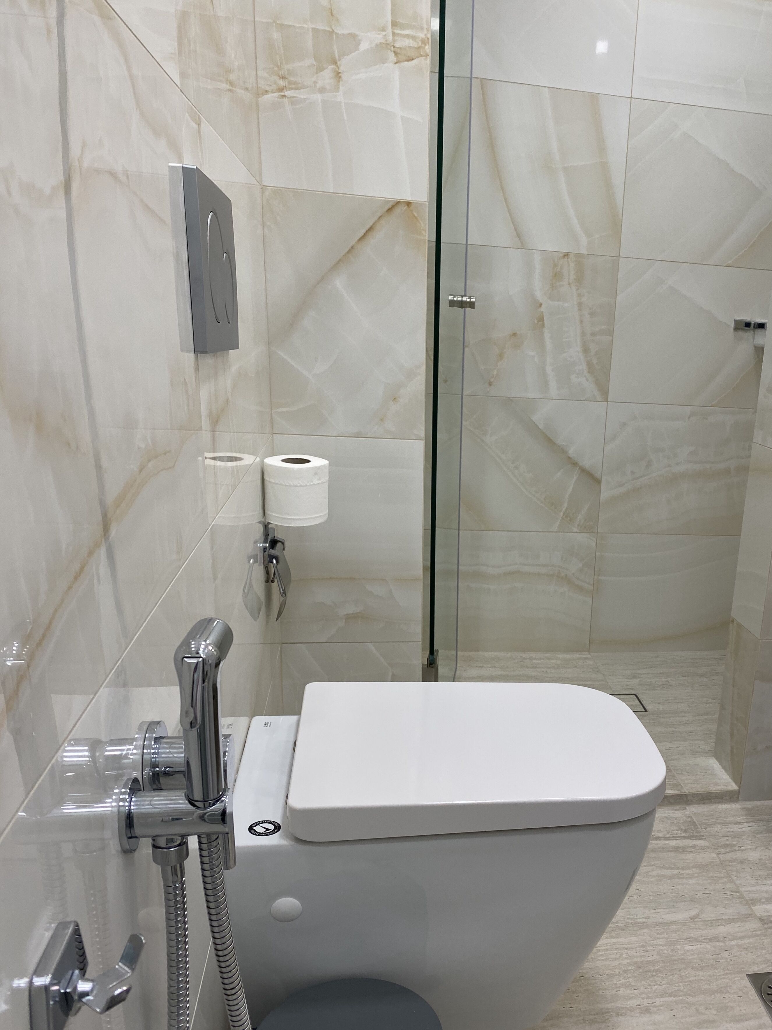 Een moderne badkamer met toilet, een douchecabine van glas en marmeren wanden.