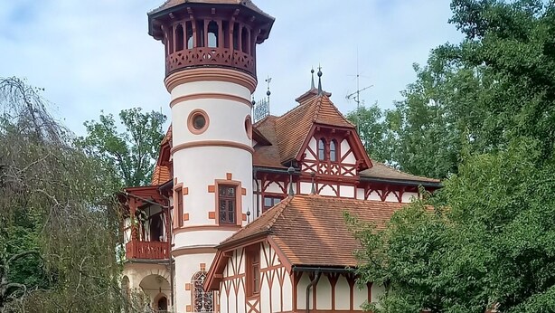 Un edificio histórico con una torre, rodeado de un jardín bien cuidado con flores coloridas.