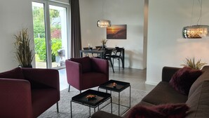A modern living room with a sofa, armchairs, and a dining area with a table and chairs. - Eilers, Katja Lilly, Ferienwohnung Lilly - Ferienwohnung Lilly (Varel)