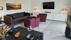 A modern living room with a sofa, armchairs, a coffee table, and a TV. - Eilers, Katja Lilly, Ferienwohnung Lilly - Ferienwohnung Lilly (Varel)