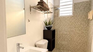Une salle de bain moderne avec un lavabo blanc, des toilettes, un espace douche et un luminaire suspendu.