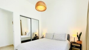 Une chambre à coucher avec un grand lit, un miroir, des tables de chevet et un luminaire suspendu.