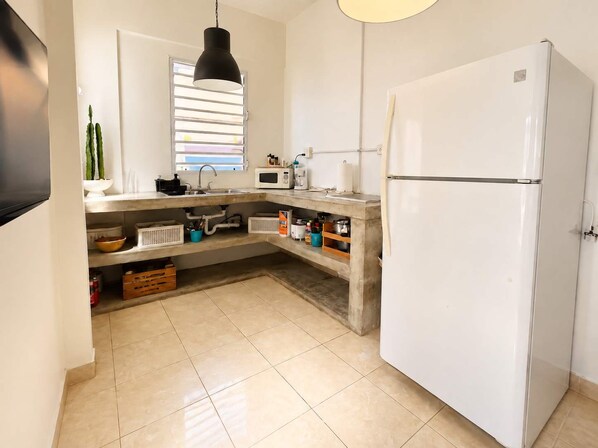 A kitchen with a white refrigerator, a microwave, a sink, and a window with blinds.