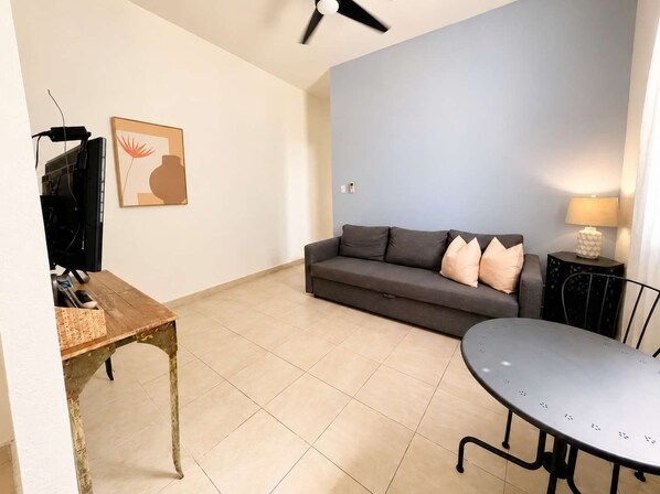 Een woonkamer met een bank, een tafel, een televisietoestel en een plafondventilator.
