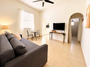 A living room with a sofa, a TV on a stand, a dining table with chairs, and a ceiling fan.
