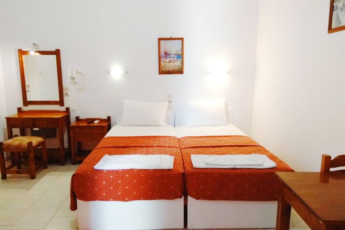 A hotel room with a double bed, a desk, a chair, a nightstand, a mirror, and a painting on the wall.