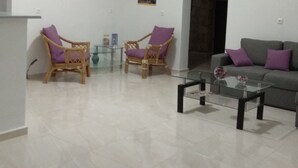 A spacious living room with a glass coffee table, two wicker chairs with purple cushions, a grey sofa with purple cushions, and a painting on the wall. - Villa Giorgos (Platanias)