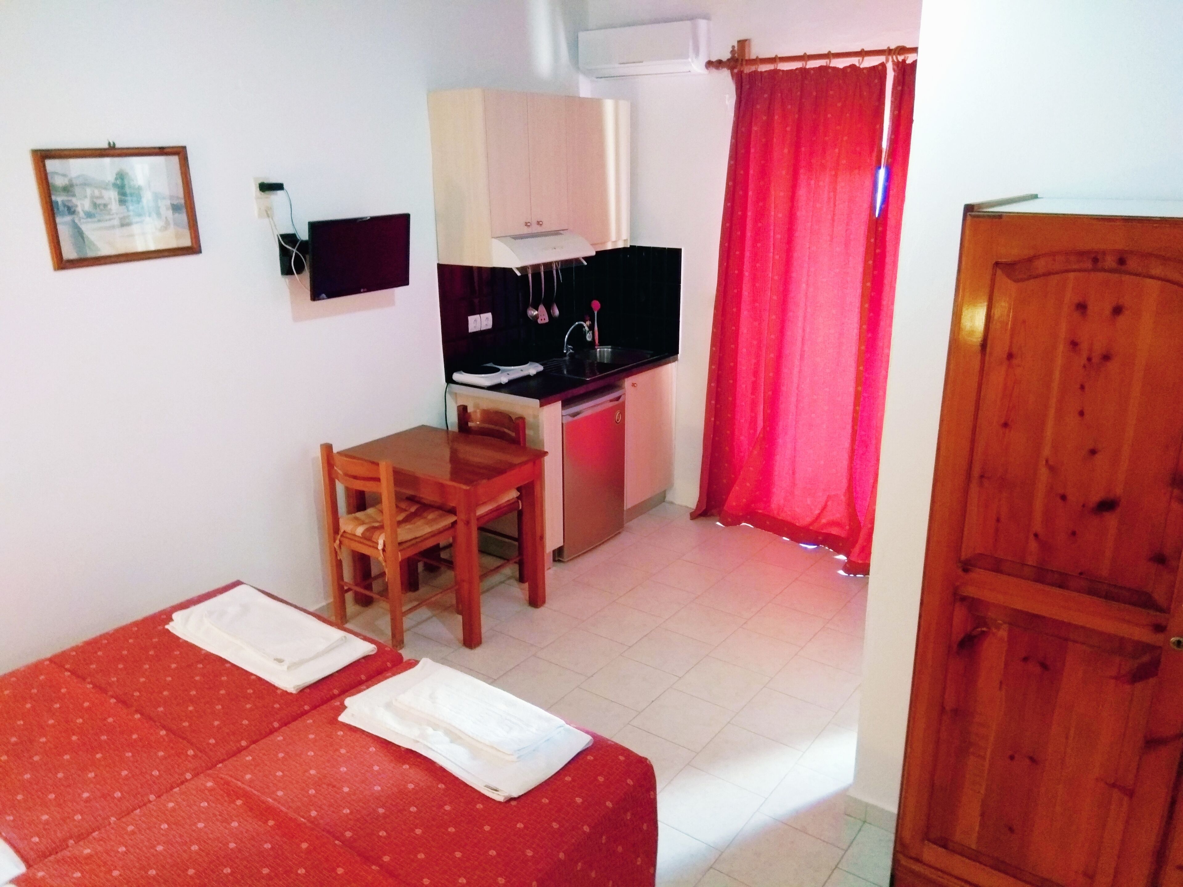 Una habitación pequeña con una cama, un escritorio, un televisor y una cortina roja.