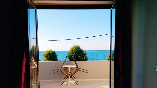 A balcony with a table and chairs, overlooking a body of water and greenery. - Villa Giorgos (Platanias)