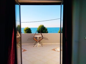 A balcony with a table and chairs, overlooking a body of water and greenery. - Villa Giorgos (Platanias)