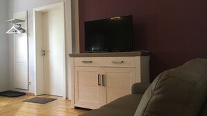 A living room with a beige sofa, a television on a cabinet, and a door leading to another room. - "elise" Apartments Nr.1 2019 Hochwertig Eingerichtetes Apartment (Mücheln (Geiseltal))
