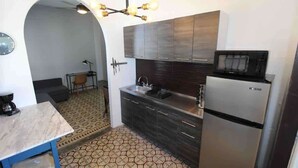 A compact kitchen with dark cabinets, a microwave, a refrigerator, a patterned floor, and a small dining area with a table and chairs. - A2-Quaint 1B-Fast WiFi-Walk to Restaurants, Beach (San Juan)