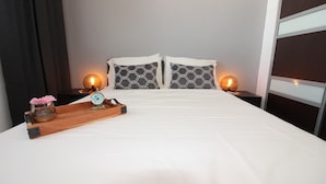 A hotel room with a large bed, two bedside tables with lamps, a wooden tray with a clock and a vase, and a window with a view. - A2-Quaint 1B-Fast WiFi-Walk to Restaurants, Beach (San Juan)