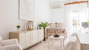 A bright, minimalist living room with a sofa, a dining table with chairs, a cabinet, and a large window with curtains. - Beautiful apt 2 rooms Cathedral views cn WIFI (Sevilla)