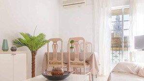 A minimalist hotel room with a bed, a small table with a bowl, two chairs, a potted plant, and a view of a building through the window. - Beautiful apt 2 rooms Cathedral views cn WIFI (Sevilla)