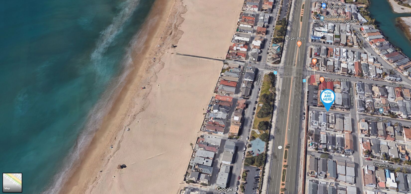 An aerial view of a coastal town with a beach, roads, and buildings.