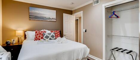 A hotel room with a bed, bedside table, lamp, and a view of a closet with hangers.