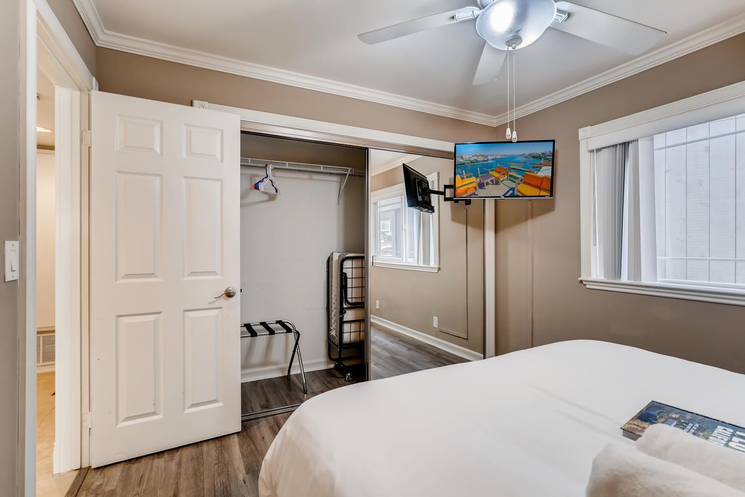 A bedroom with a bed, a ceiling fan, a TV mounted on the wall, and a window with blinds.