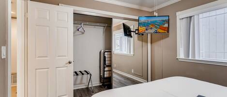A bedroom with a bed, a ceiling fan, a TV mounted on the wall, and a window with blinds.