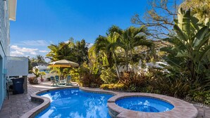 A swimming pool with a hot tub, surrounded by lush tropical plants and a patio area with outdoor furniture. - Beach Bay Serenity: Pine Ave canal front pool home (Anna Maria)