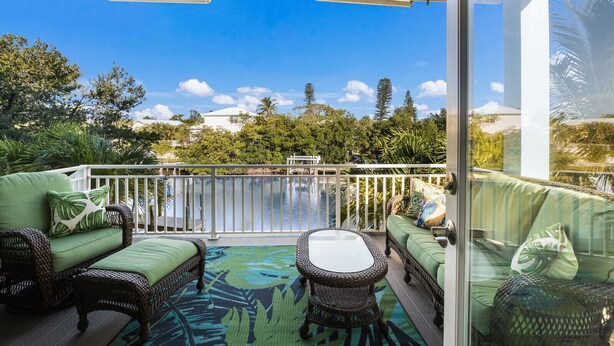 A covered outdoor seating area with wicker furniture and a view of a pool and trees. - Beach Bay Serenity: Pine Ave canal front pool home (Anna Maria)