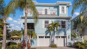 A two-story house with a light blue exterior, white shutters, and a front porch. - Beach Bay Serenity: Pine Ave canal front pool home (Anna Maria)