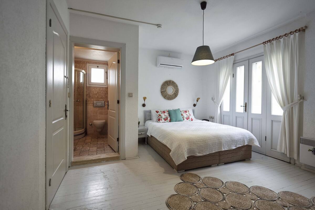 A bedroom with a bed, bedside table, and a view of the bathroom.