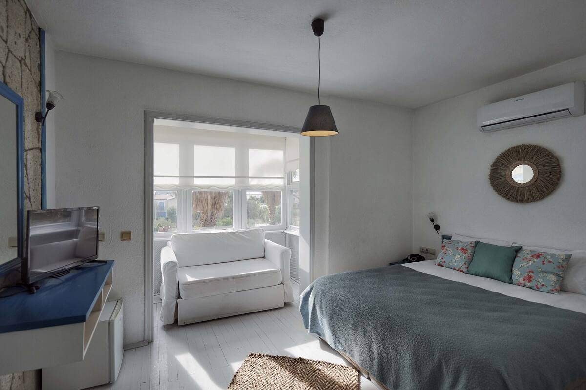 A bedroom with a bed, a desk with a computer, a window, and an air conditioner.