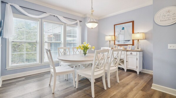A dining area with a round table, white chairs, a vase of flowers, and a wall-mounted lamp.