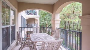 A balcony with a table and chairs, overlooking a garden and a building with outdoor furniture.