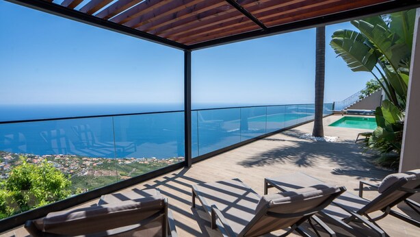 A balcony with a glass barrier overlooking a coastal view, including a swimming pool and a distant cityscape. - Mansão Macau by LovelyStay (Arco Da Calheta)