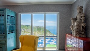 A room with a large sliding glass door leading to a scenic view, a yellow armchair, a turquoise cabinet, and a statue on a red cabinet. - Mansão Macau by LovelyStay (Arco Da Calheta)