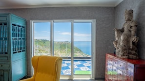 A room with a large sliding glass door leading to a scenic view, a yellow armchair, a turquoise cabinet, and a statue on a red cabinet.