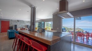 A modern kitchen with a large island, red bar stools, and a view of the ocean. - Mansão Macau by LovelyStay (Arco Da Calheta)