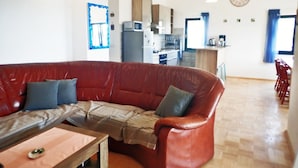 Een woonkamer met een rode leren bank, een houten salontafel en een keuken op de achtergrond.