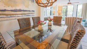 A dining area with a glass table, woven chairs, and a chandelier.