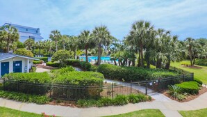 A hotel with a pool, palm trees, and a fenced garden area.