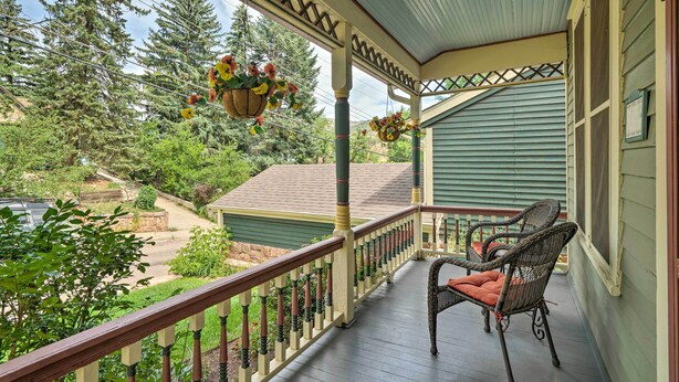 A porch with wicker furniture and hanging flower baskets. - Historic Manitou Springs Victorian: Walk Downtown! (Manitou Springs)