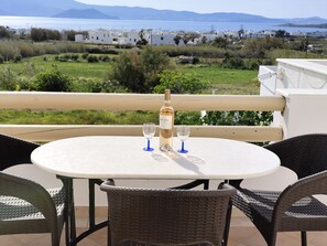 A round table with a bottle of white wine and two glasses on a balcony overlooking a coastal view with buildings and greenery.