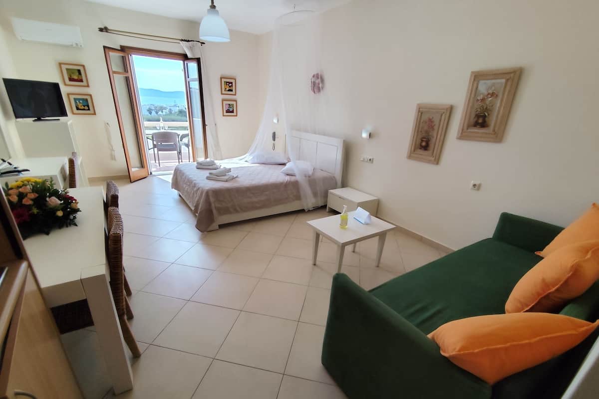 A hotel room with a bed, a green sofa, a small table, and a balcony with a view.