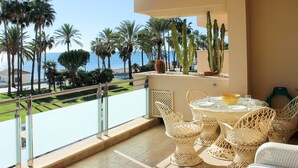 A balcony with wicker furniture, a glass table, and a view of the sea and palm trees. - First floor Beach side property, San Pedro (Marbella)