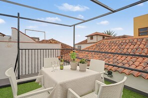 Eine Dachterrasse mit einem für zwei Personen gedeckten Tisch, zwei Kübelpflanzen und einer Weinflasche.