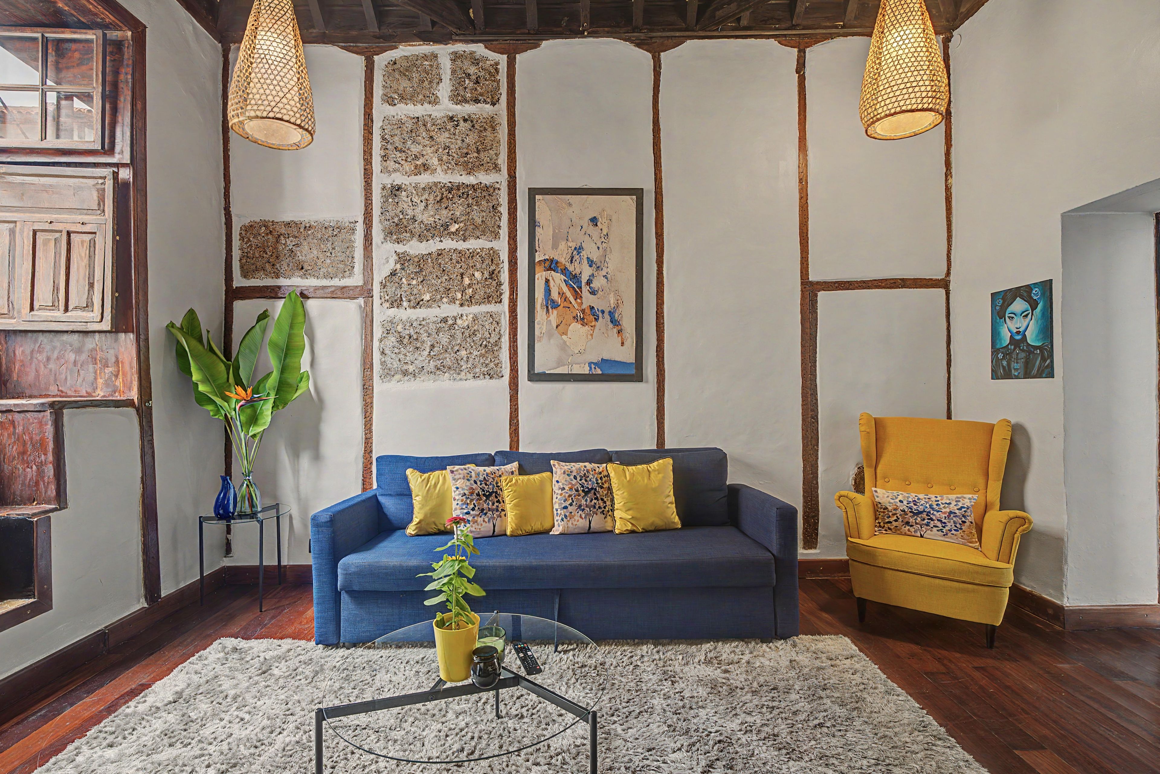 A room with a blue sofa, a yellow armchair, a coffee table, and a large plant.