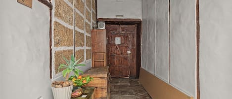 A narrow hallway with a wooden door, a table with a plant and fruit basket, and a wall with a 'SALIDA' sign.