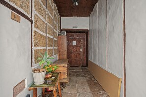 Ein schmaler Flur mit einer Holztür, einem Tisch mit Pflanze und Obstkorb sowie einer Wand mit dem Schild 'SALIDA'.