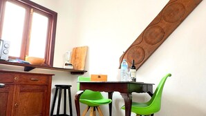 Une cuisine avec des meubles de rangement en bois, une table à manger avec des chaises, un luminaire suspendu et une fenêtre.
