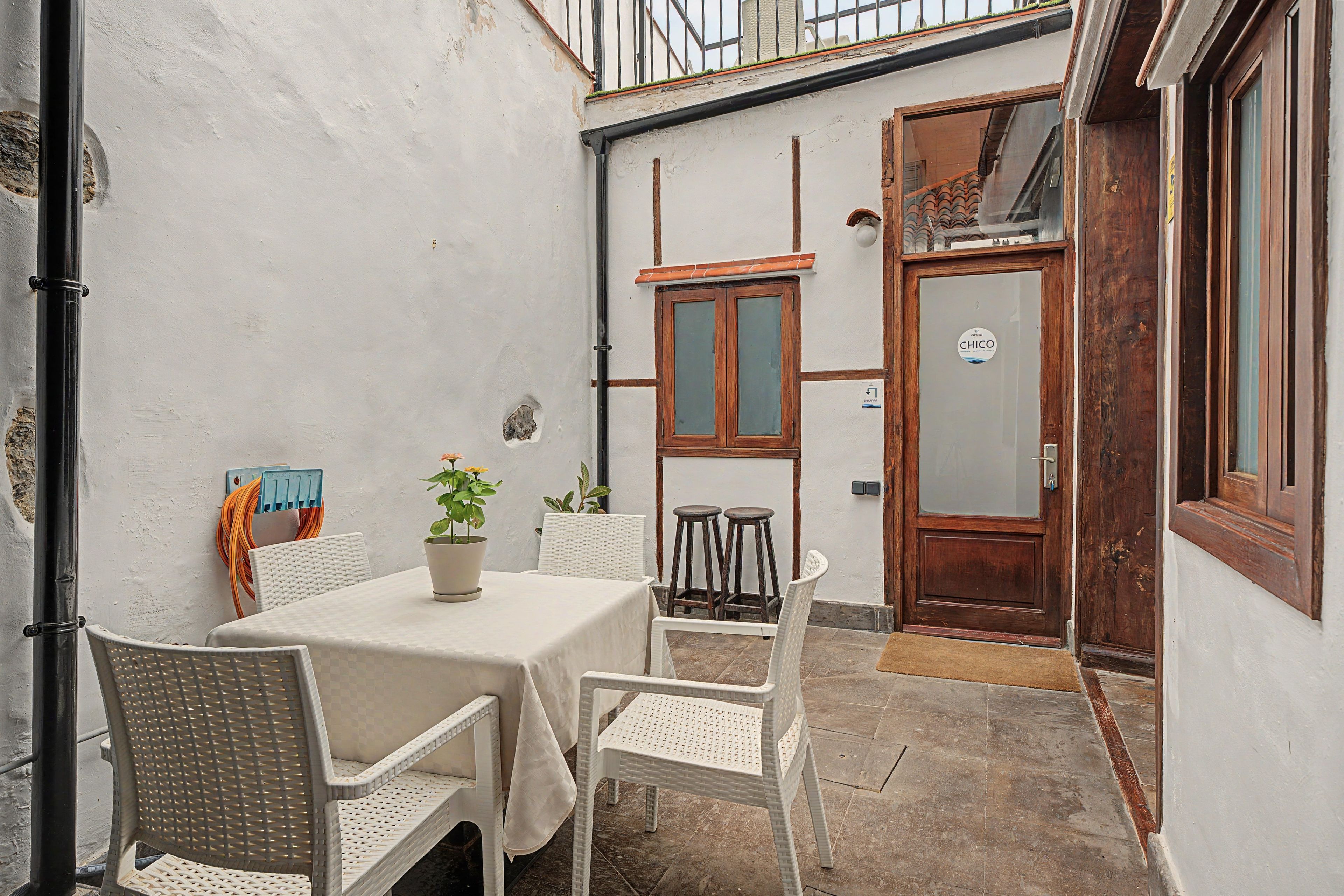 Un pequeño patio al aire libre con una mesa, sillas, una planta en maceta y una puerta de madera.