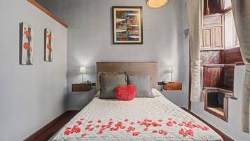 A bedroom with a bed, two bedside tables, a nightstand, a wall-mounted lamp, and a window with curtains.