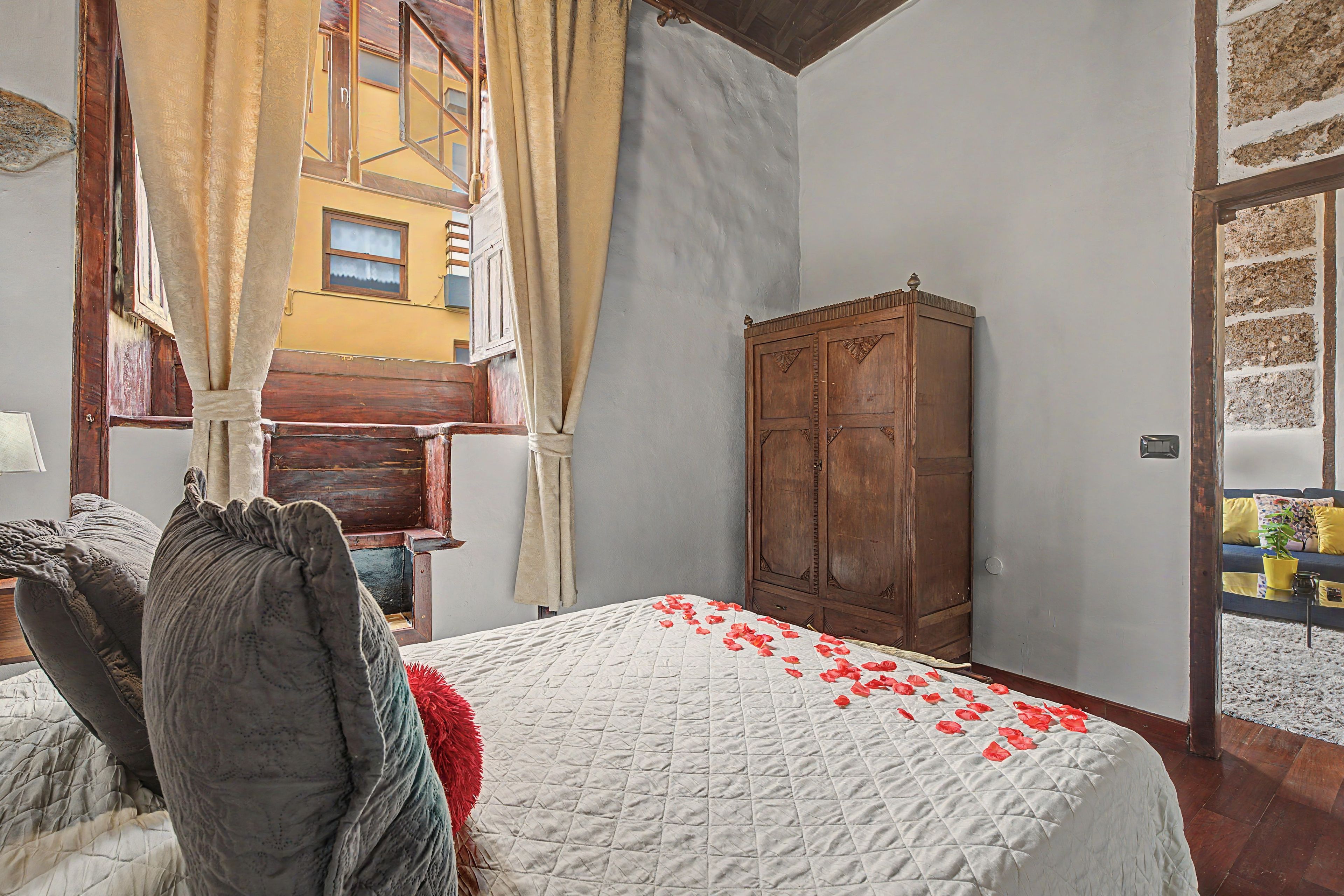 Een slaapkamer met een bed, een houten kledingkast en een raam met gordijnen.